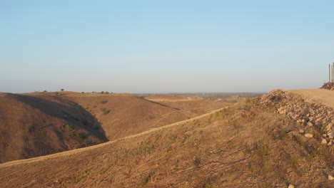 forward along dirt road reveal shot of valley between barren and dry hills at golden hour in algarve, portugal