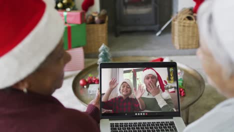 diversas amigas mayores que usan una computadora portátil para una videollamada de navidad con una familia feliz en la pantalla