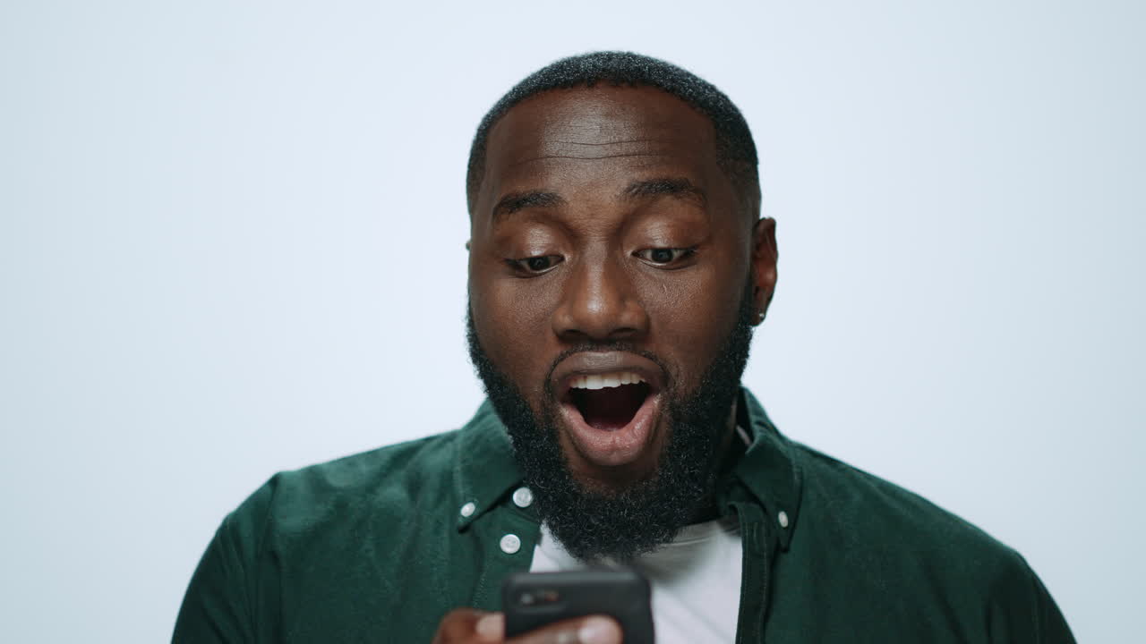 Closeup surprised african guy browsing internet online on phone in studio.