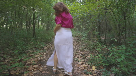 pregnant woman expectant mother walking alone in forest path surrounded by vegetation trees, pretty casual dressed mom turning around stroking touching her belly smiling, childbearing and tenderness