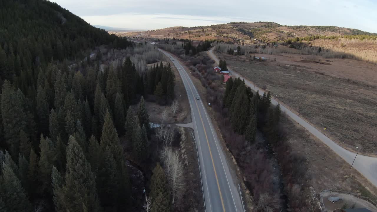 FPV footage of a road in the middle of Idaho. On the road there are few cars, trees are on one side and plains on the other