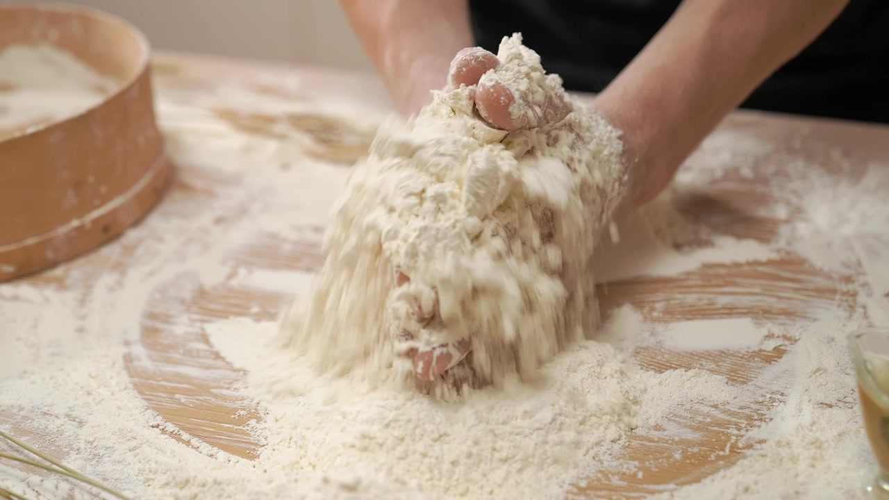 Primo piano di mani che preparano l'impasto con farina su una superficie di legno
