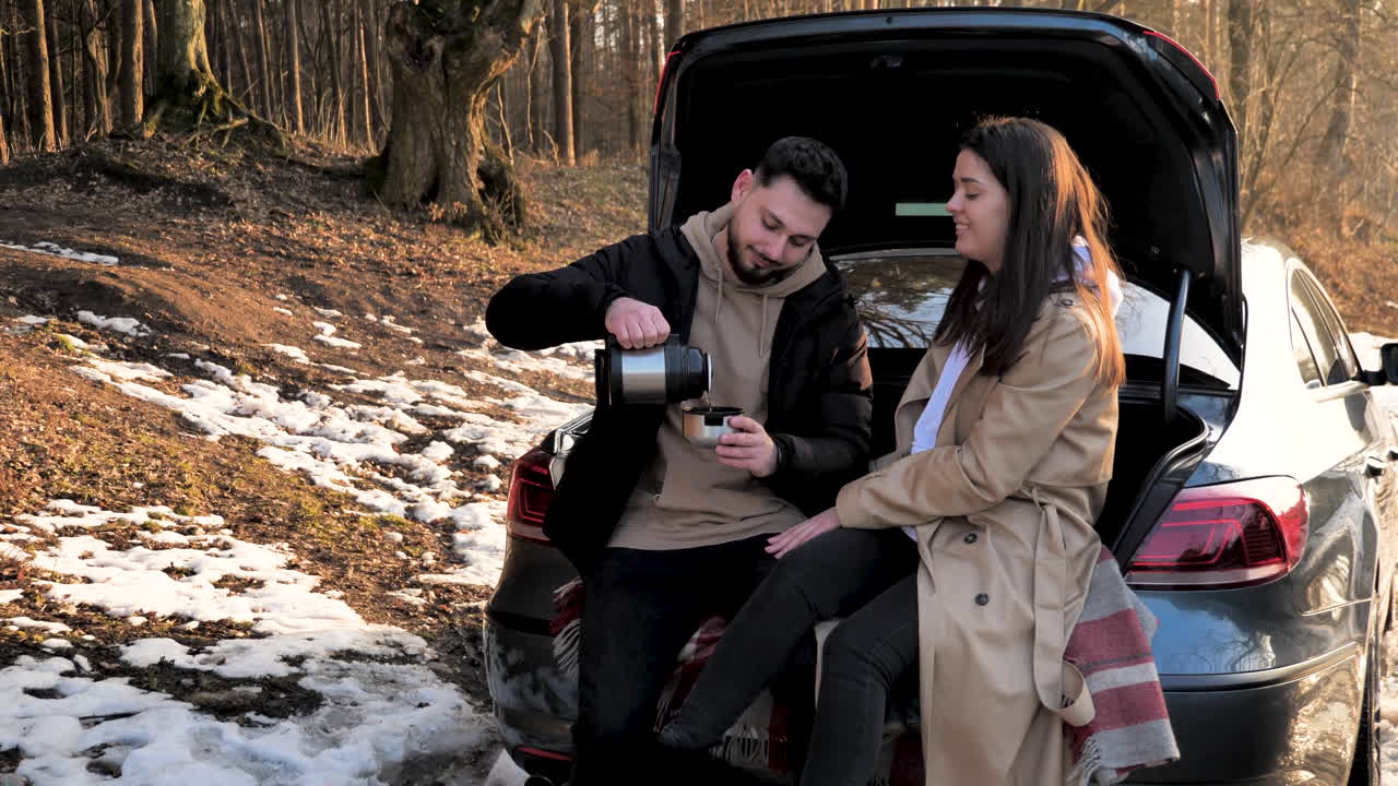 눈 덮인 숲에서 따뜻한 차를 마시고 있는 백인 커플.