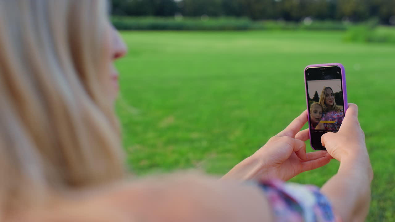 vista trasera de una mujer posando para un teléfono inteligente al aire libre. familia tomando una selfie en el parque.