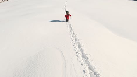 Toma-Aérea-Baja-Hacia-Un-Hombre-Aventurero-Que-Camina-A-Través-De-La-Nieve-Profunda-Con-Una-Gran-Bolsa-De-Trekking