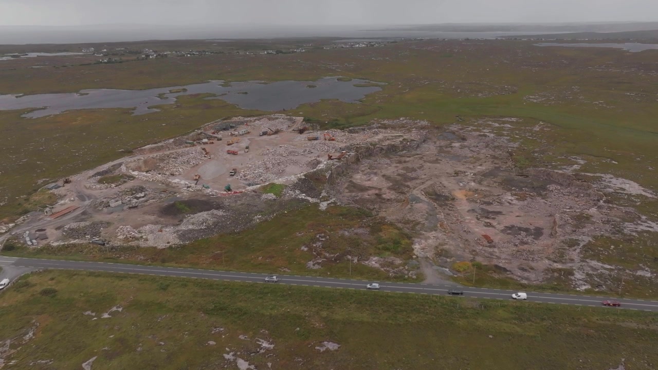 Una ripresa aerea con drone cattura una grande cava di pietra attiva nell'aspro paesaggio del Connemara, con macchinari e auto che circolano su una vicina strada principale