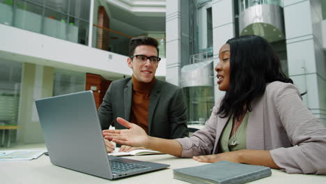 compañeros de trabajo multiétnicos usando portátiles y hablando en el centro de la oficina