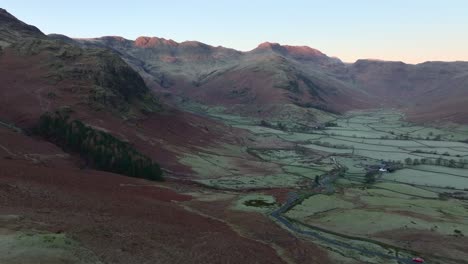 dawn light catching distant mountain tops with flight over wide valley and dead bracken. langdales, english lake district, cumbria, uk.