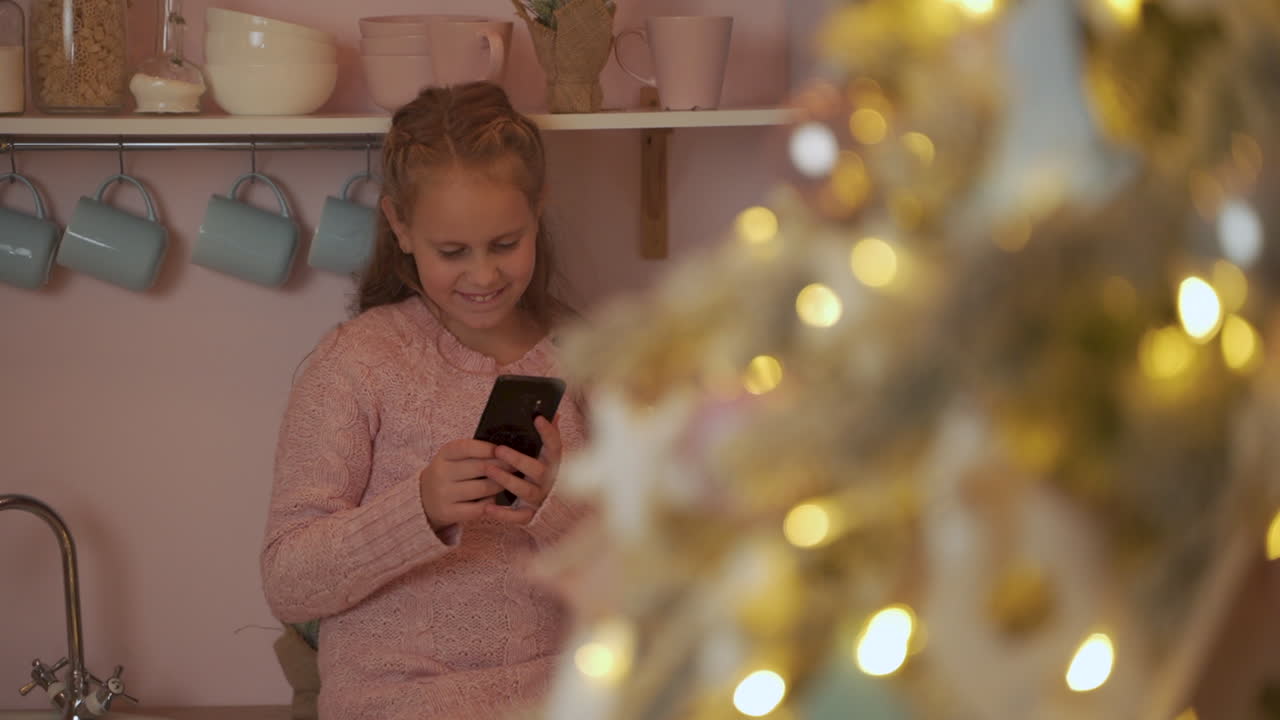 Happy Little Girl Uses Her Phone To Send Merry Christmas Messages At Home