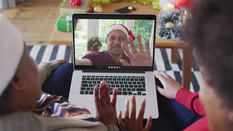 madre y hija afroamericanas usando una computadora portátil para una videollamada de navidad con un hombre en la pantalla