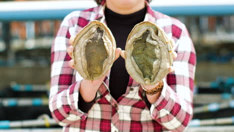 woman wearing red checkered shirt holds out and displays two large abalones