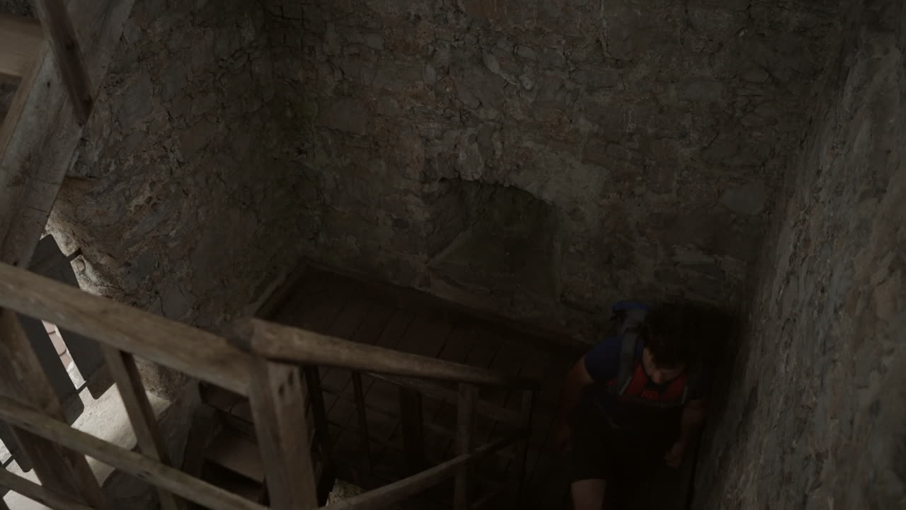 un joven excursionista con una mochila subiendo las escaleras en la antigua torre para llegar a la cima
