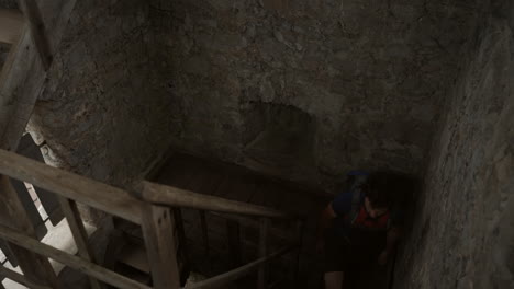 un joven excursionista con una mochila subiendo las escaleras en la antigua torre para llegar a la cima