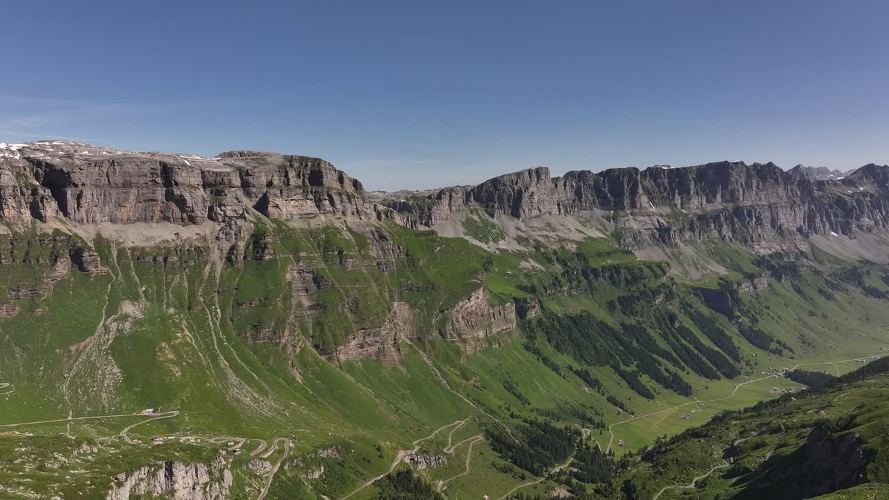 Pemandangan udara Fisetenpass dan Klausenpass di Pegunungan Alpen Swiss, menampilkan lembah hijau yang memukau, tebing berbatu, dan langit biru cerah.