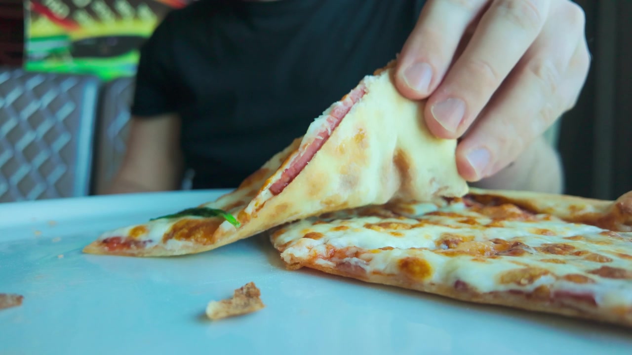 Primo piano, una fetta di pizza scompare in bocca, a simboleggiare abitudini alimentari malsane