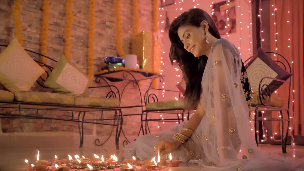 A beautiful girl in traditional sari and ornaments making a Rangoli on a floor during Diwali festival. A smiling lady drawing indian art on the floor using flower petals, Colored sand and oil lamps