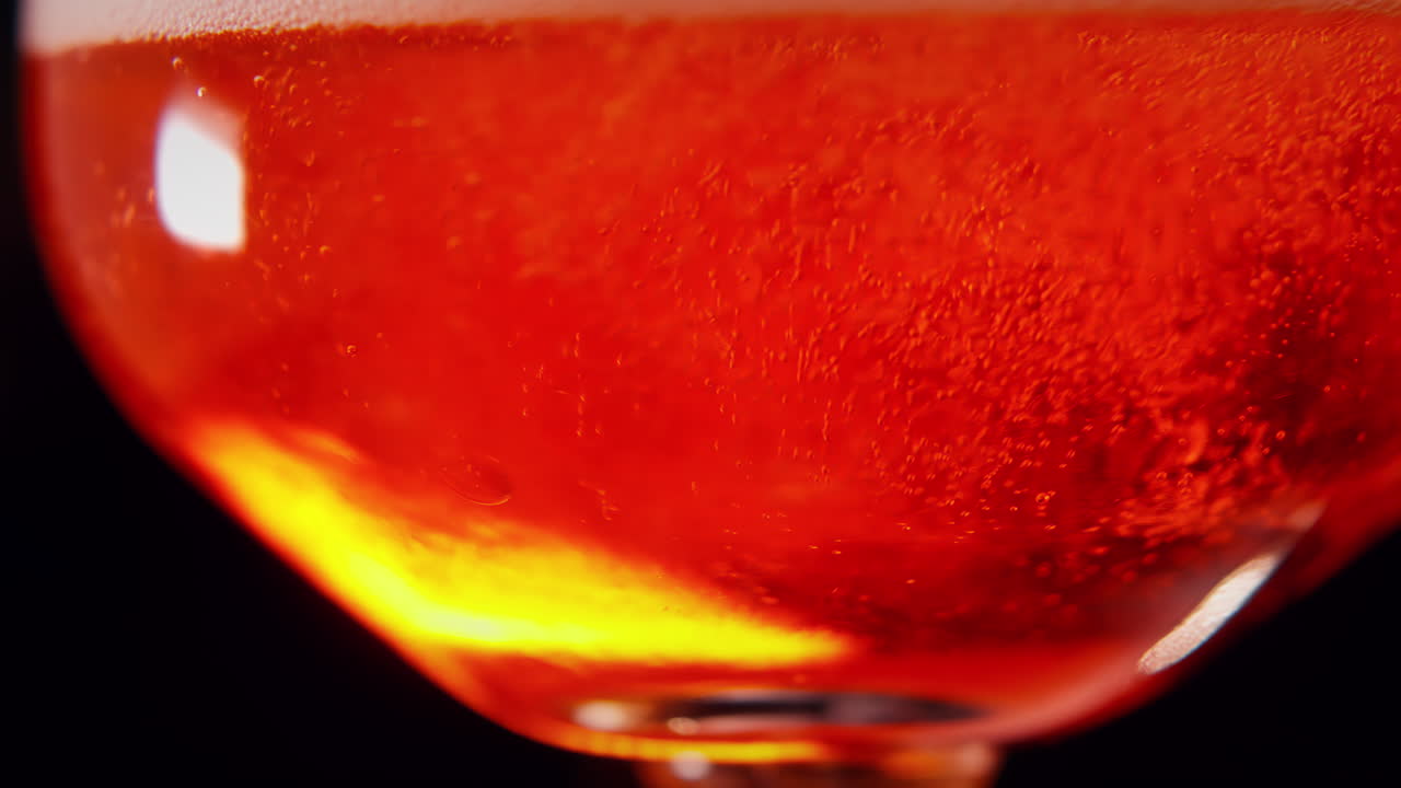 Macro inquadratura di liquido rosso con bolle spumose che salgono in superficie, ripetibile in loop e ideale per visual astratti o scientifici.