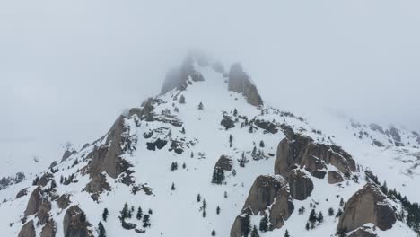 Snowy-Ciucas-Mountains-peak-shrouded-by-clouds-in-a-serene,-untouched-landscape,-aerial-view