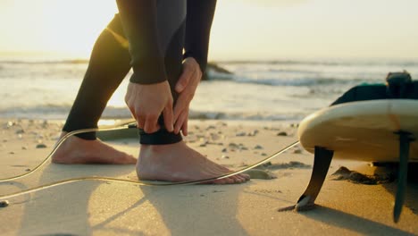 Low-section-of-mid-adult-caucasian-male-surfer-tying-surfboard-leash-at-the-beach-4k