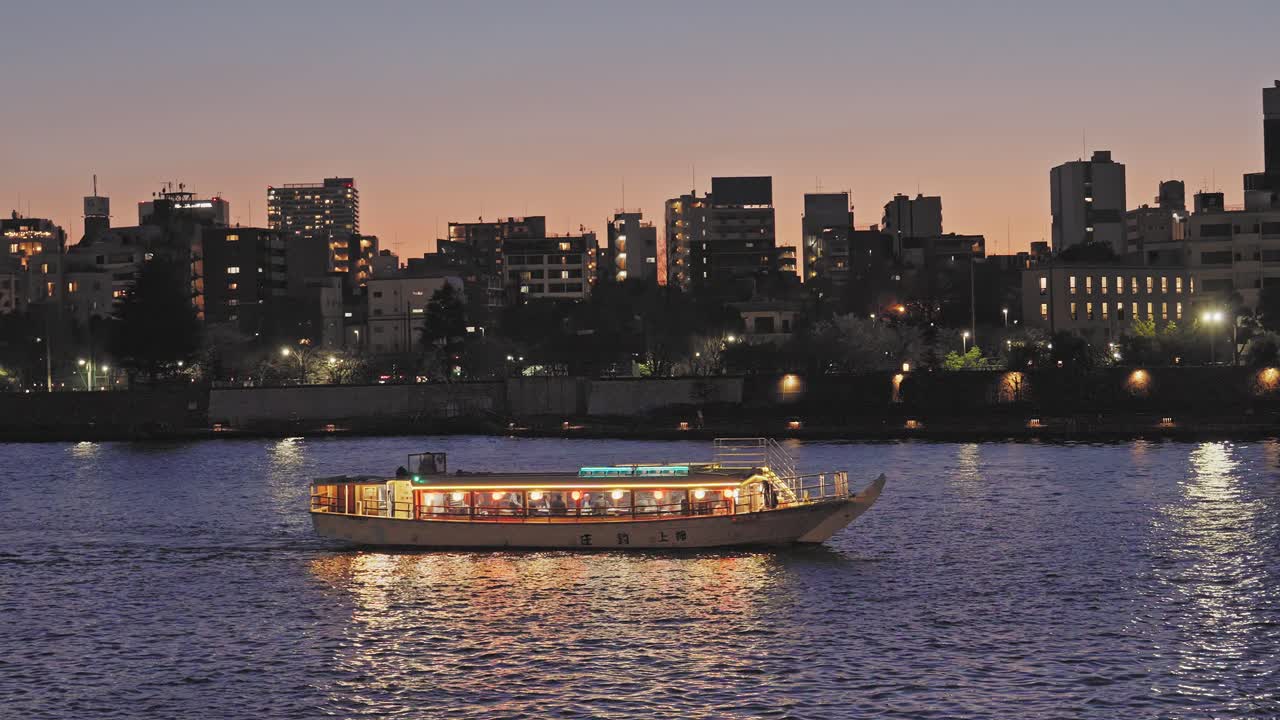 Una tradizionale barca da crociera giapponese Yakatabune risplende sul fiume Sumida al crepuscolo. Lo skyline della città crea uno sfondo scenografico in questa inquadratura cinematografica.