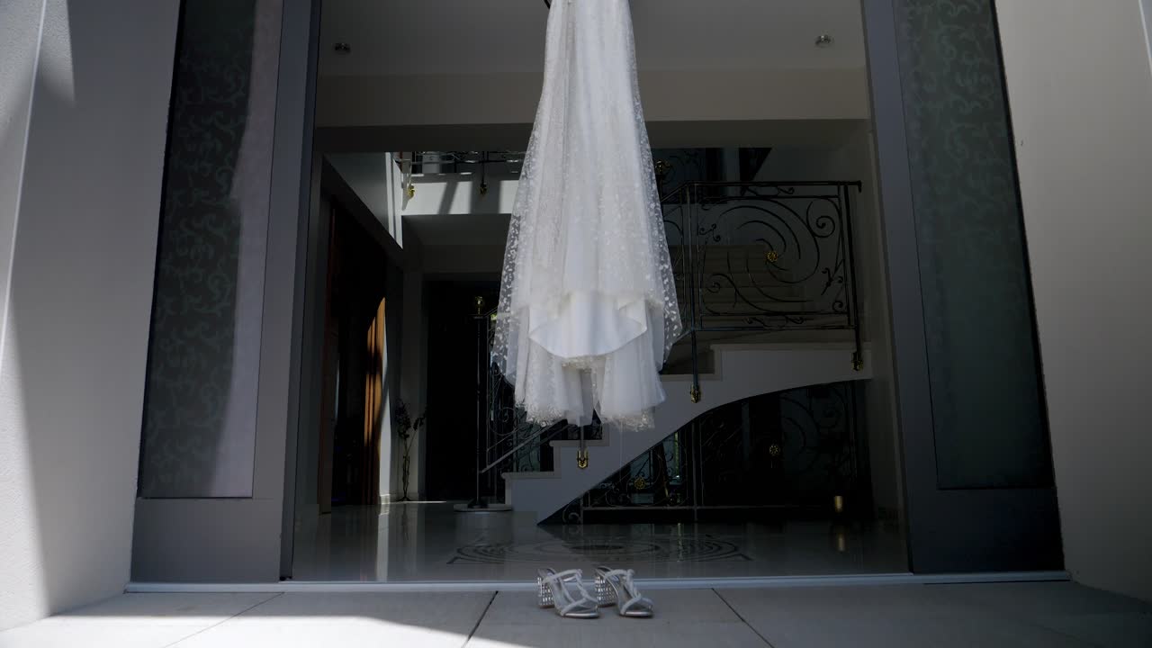 웨딩 드레스와 그녀의 신발이 고급스러운 집 입구에 매달려 있습니다. 결혼식이 준비되고 있습니다.