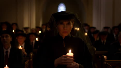 Woman in black veil holding a candle in a solemn gathering