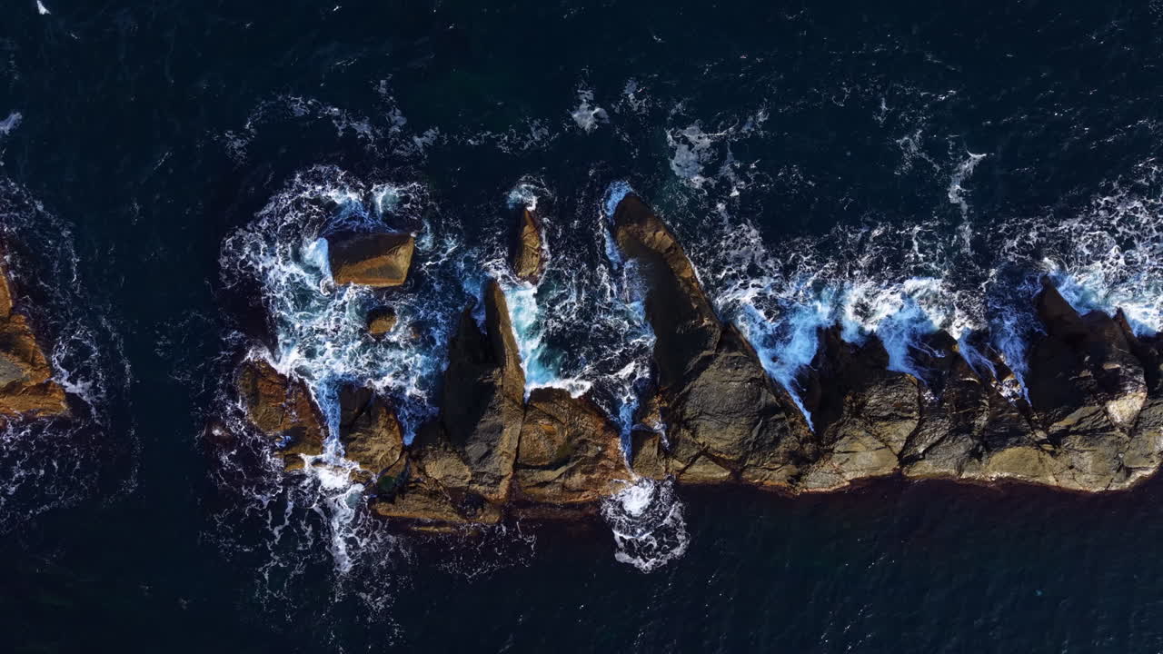 Waves crash against rugged rocks at sunset, creating a dynamic scene of nature's power and beauty along the coast