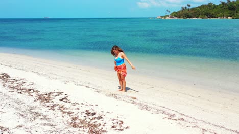 Atractiva-Mujer-Deportiva-Haciendo-Ejercicios-De-Yoga-En-Una-Playa-De-Arena-Blanca-Bañada-Por-Una-Hermosa-Laguna-Turquesa-En-La-Bahía-De-La-Isla-Tropical,-Tailandia