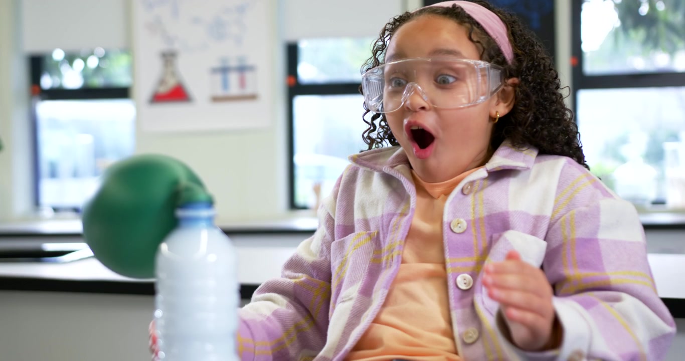 African American child fitting balloon onto bottle in school lab, goggles on, showing foam reaction