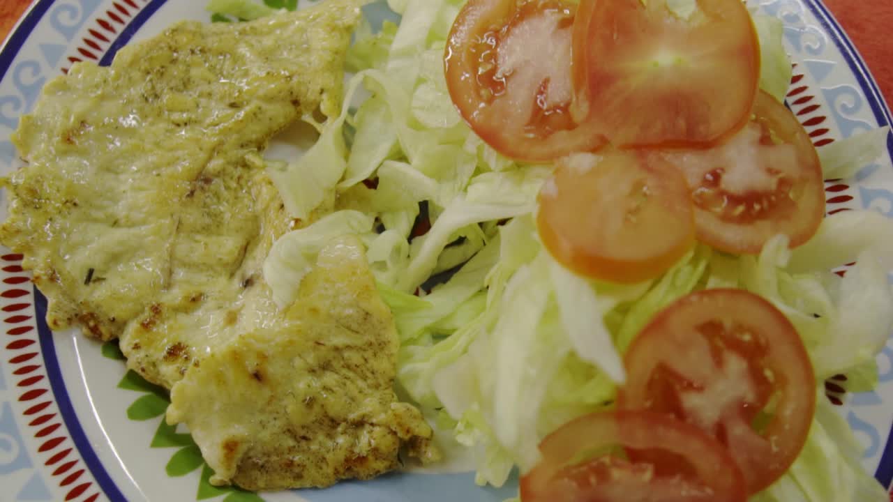 Pollo alla griglia con lattuga e pomodoro su un piatto colorato.