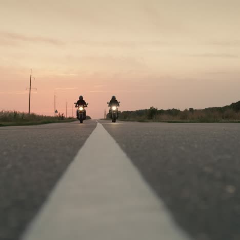 Two-motorcycles-drive-on-a-flat-highway-at-sunset