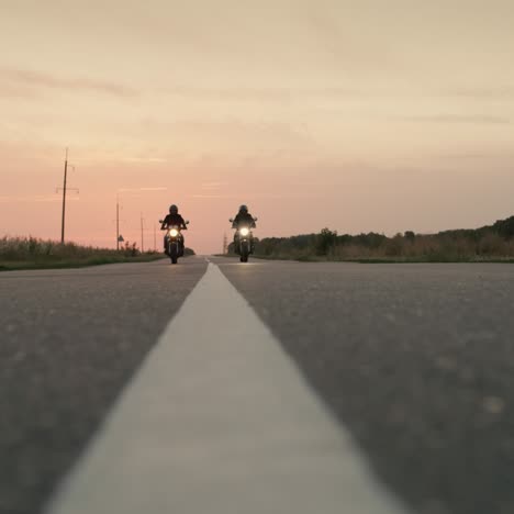 two motorcycles drive on a flat highway at sunset