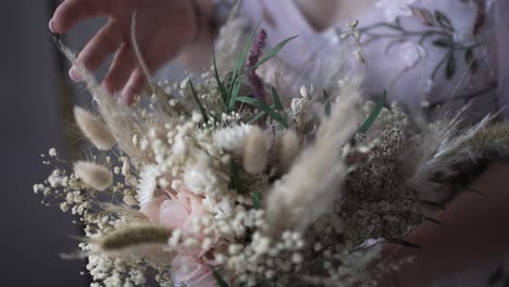 close up of hand brushing delicate wedding bouquet of dried wildflowers