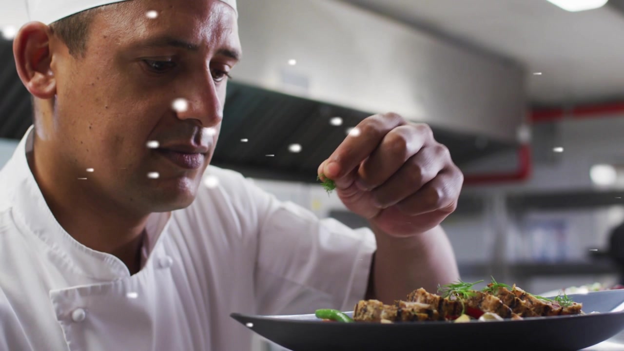 Chef uomo che ispeziona e aggiunge una guarnizione di erbe aromatiche per il servizio in cucina, con bokeh bianco che evidenzia il piatto.