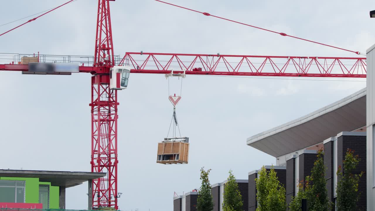 Red construction tower crane swings materials to highrise work site