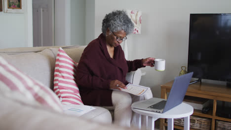 una mujer afroamericana de edad avanzada bebiendo café mientras calcula las finanzas en casa.