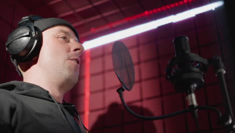 close-up of a man dressed in black, passionately singing into a microphone in a soundproofed recording room. the singer is wearing headphones and making expressive hand movements