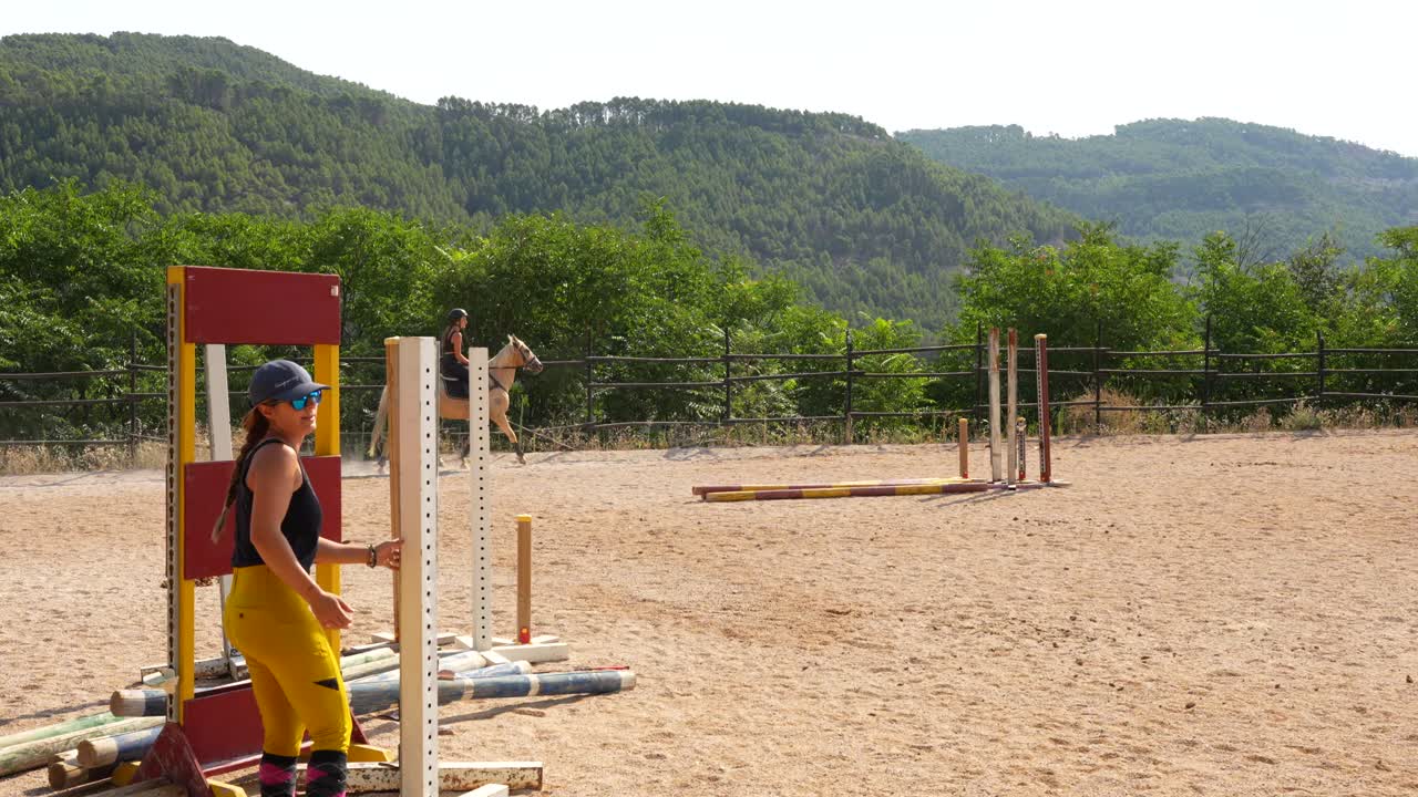 Horse riding trainer prepares hurdles on the track as a rider circles behind to keep warm before attempts