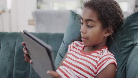 Happy-african-american-girl-sitting-on-sofa,-using-tablet,-slow-motion