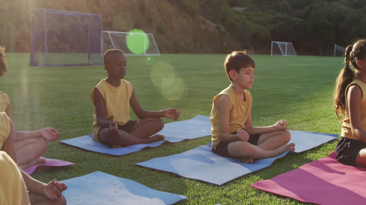 grupo diverso de escolares sentados en esteras meditando durante una lección de yoga al aire libre