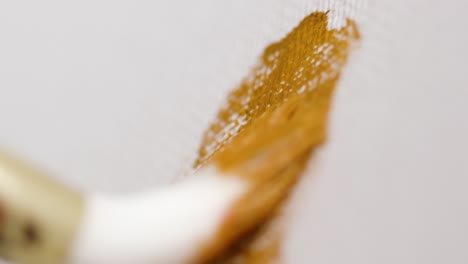 close-up of applying golden paint to canvas with a brush