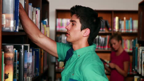 estudiante guapo escogiendo un libro en la biblioteca