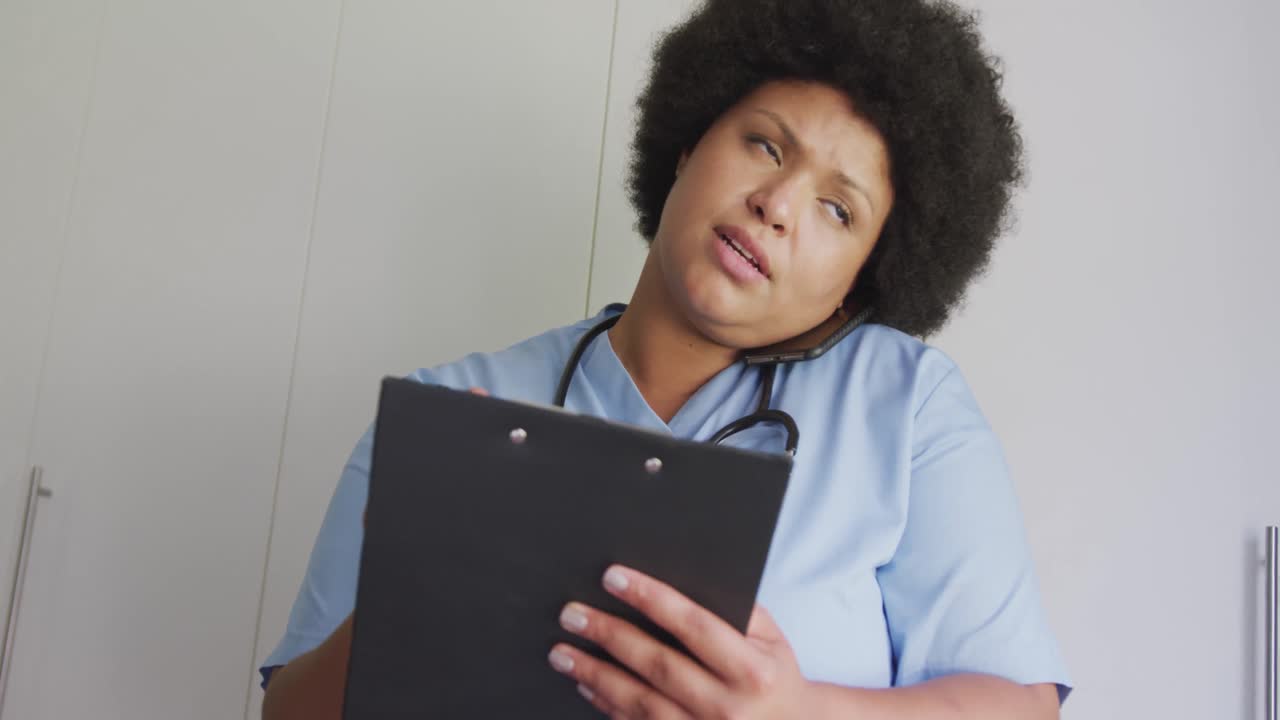 video de una doctora afroamericana de tamaño grande enfocada usando un teléfono inteligente y una tableta