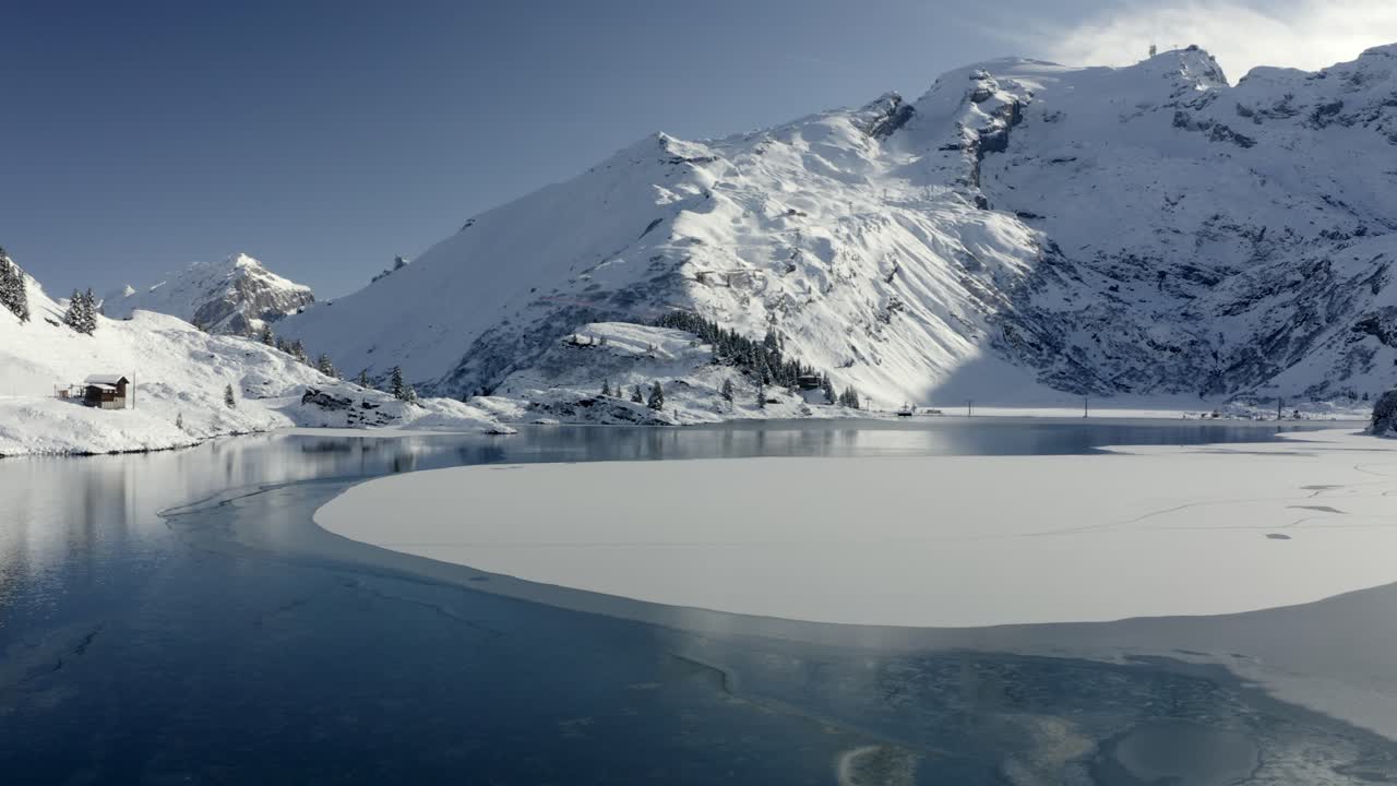 Aerial footage, slow descent over freezing lake in winter landscape with lots of snow at Trübsee in Switzerland