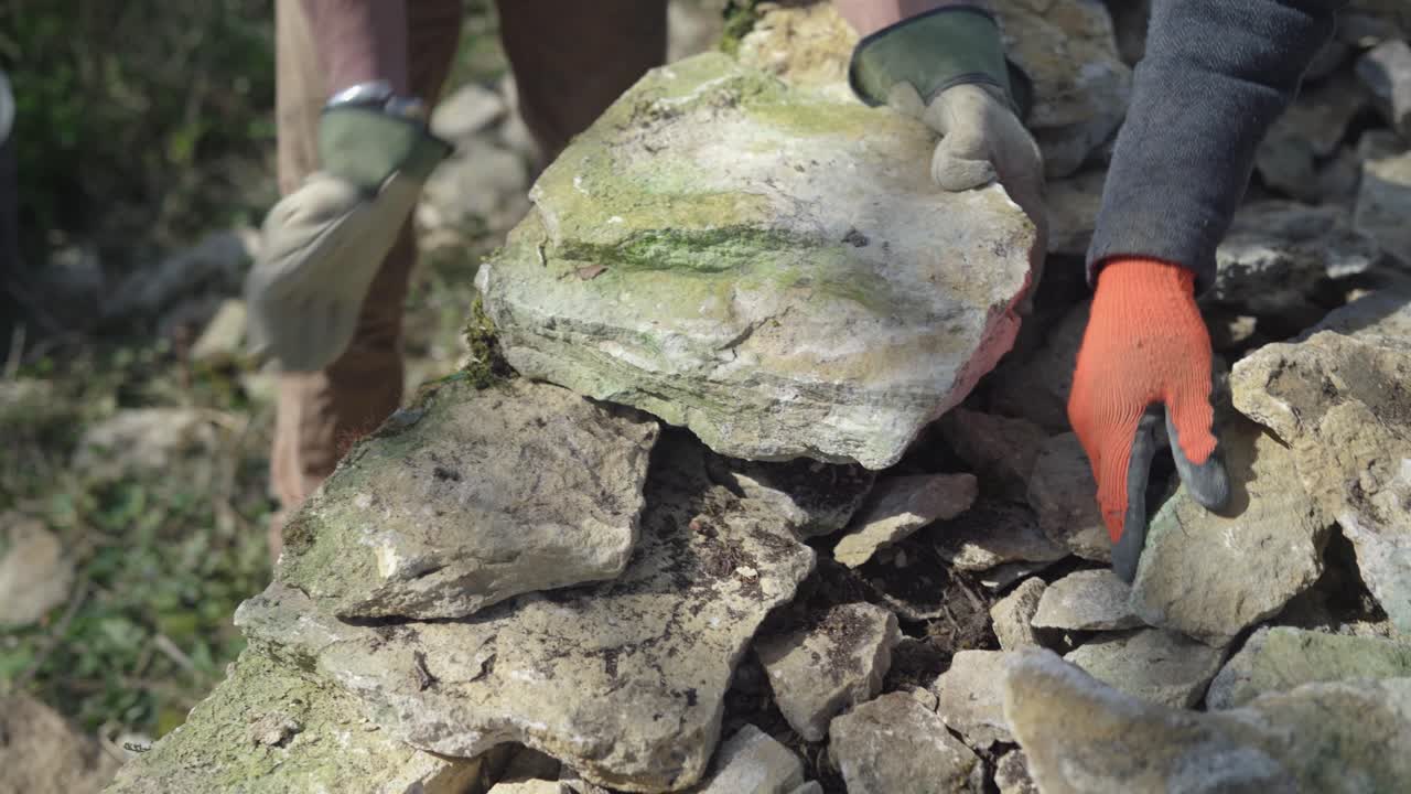 dos hombres construyendo un muro de piedra seca, colocando piedras para hacer un muro