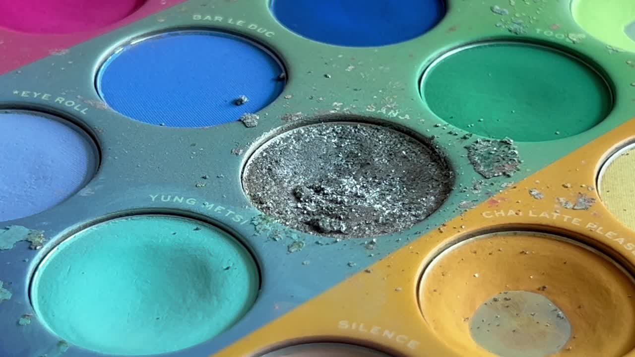 un pincel se sumerge en un color de una paleta de colores y recoge algo de color - primer plano de una paleta de colores para maquillaje