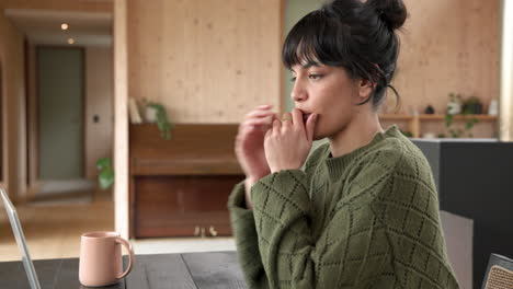 at home, woman in green sweater using laptop and holding coffee mug