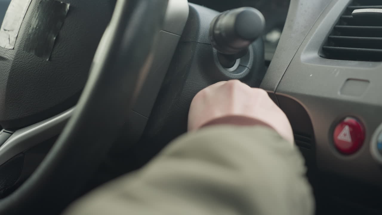 close up of person inserting car key into ignition and leaving it inside keyhole, dashboard and steering wheel visible in frame, moment captures subtle action inside vehicle with interior details