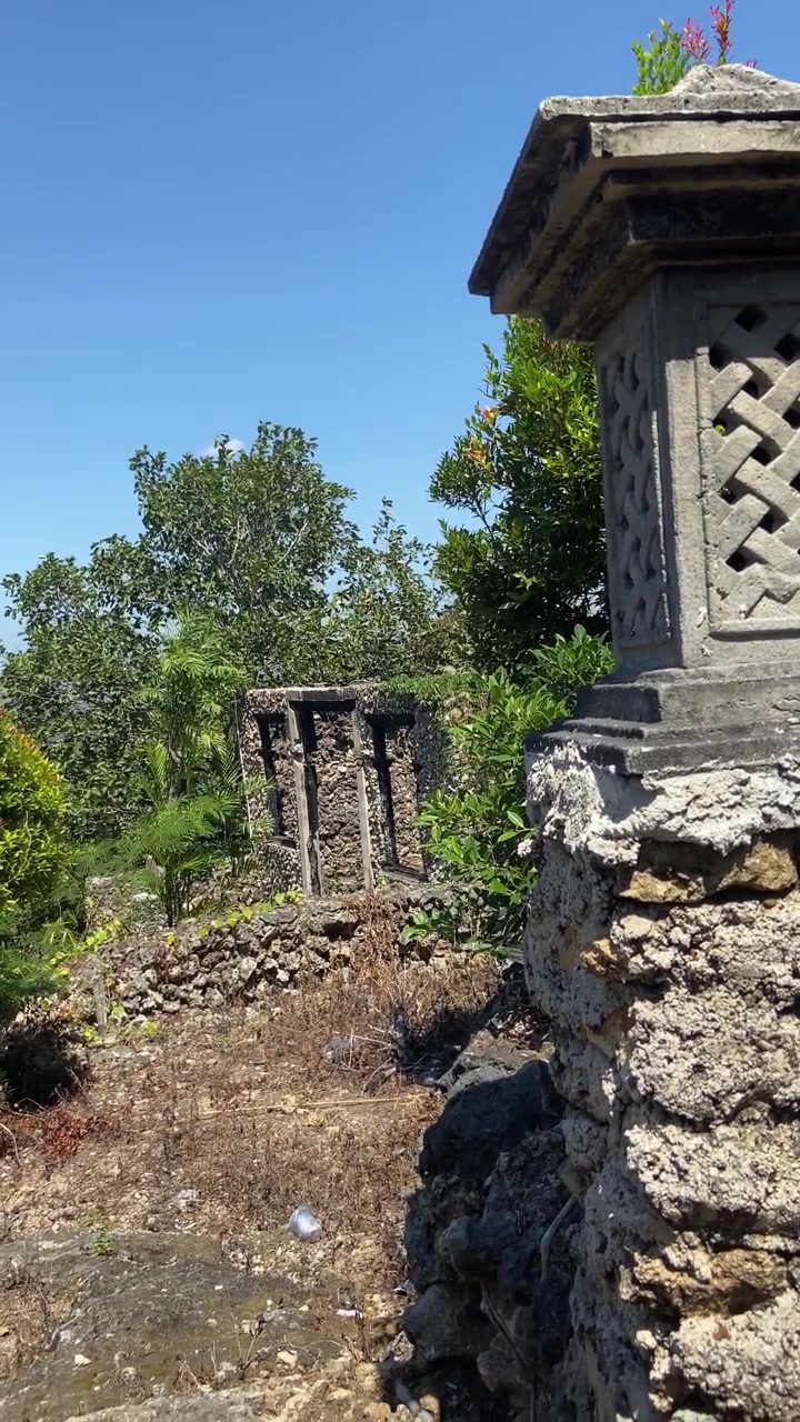 Lanterna di pietra consumata dalle intemperie che si affaccia su rovine invase dalla vegetazione in una giornata di sole
