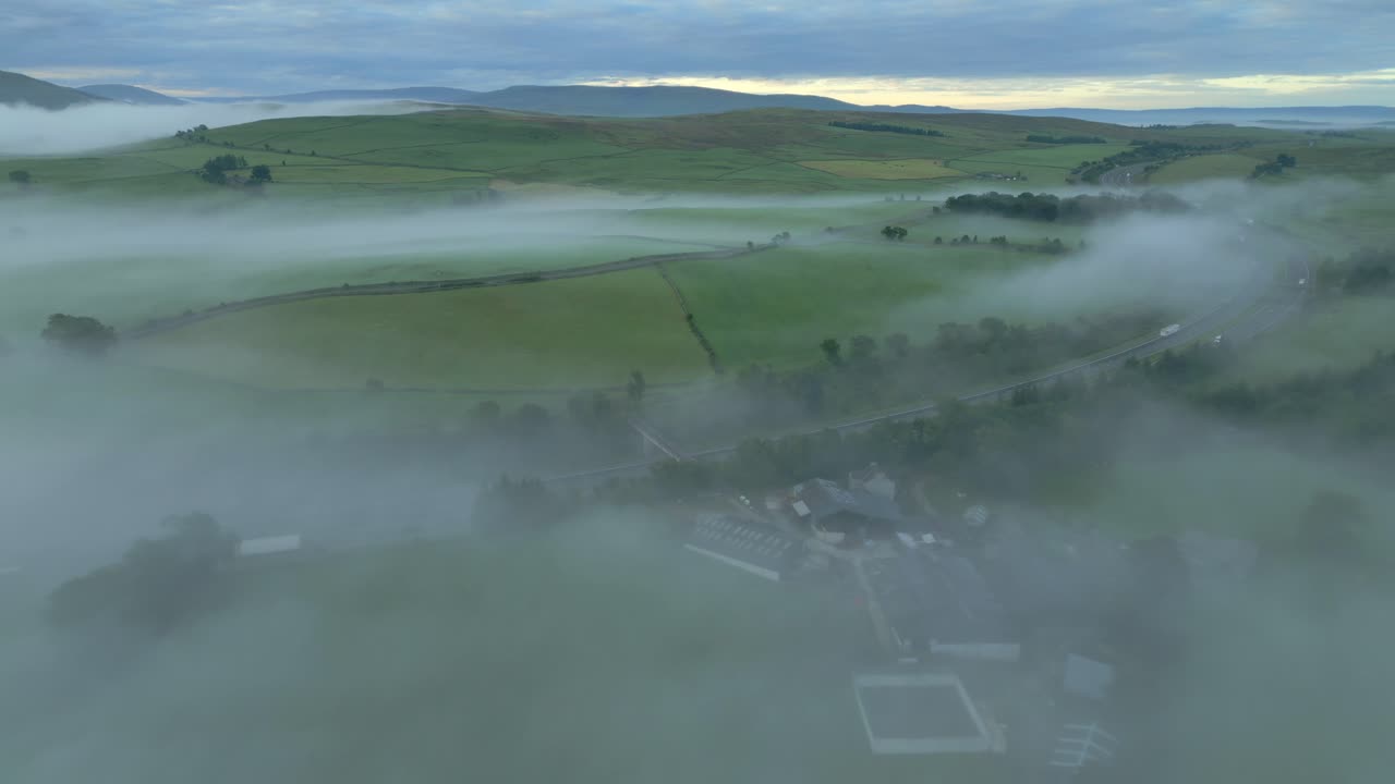 m6 고속도로를 향해 날아가며, 해가 뜨면 먼 곳의 초록색 언덕과 함께 안개에 여 있습니다.